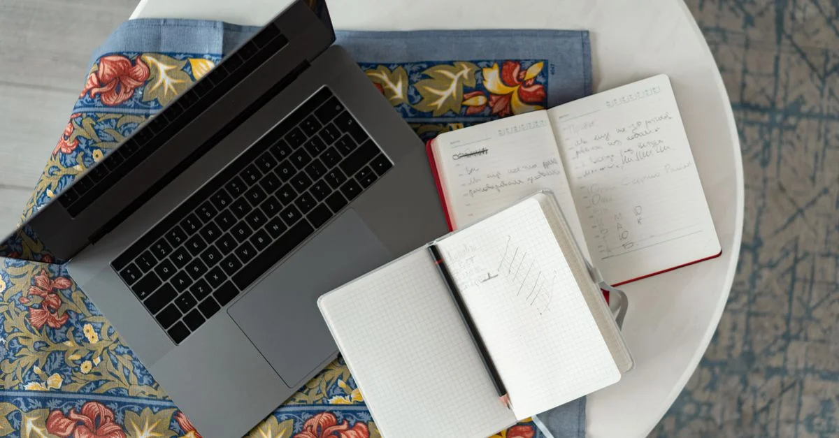 Vue de dessus d'un ordinateur portable avec des blocs-notes et un crayon sur un tissu à motifs.