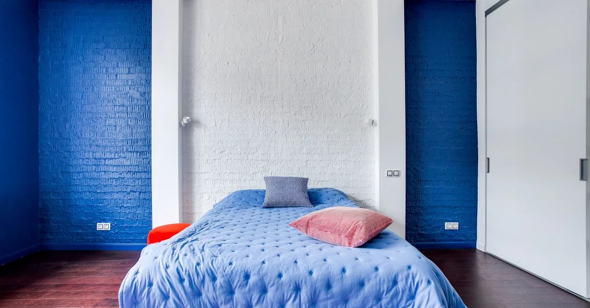 Chambre moderne avec des murs bleu marine, un lit confortable et des coussins élégants.
