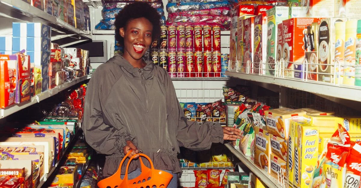 Femme souriante faisant ses achats dans un rayonnage rempli de produits colorés.