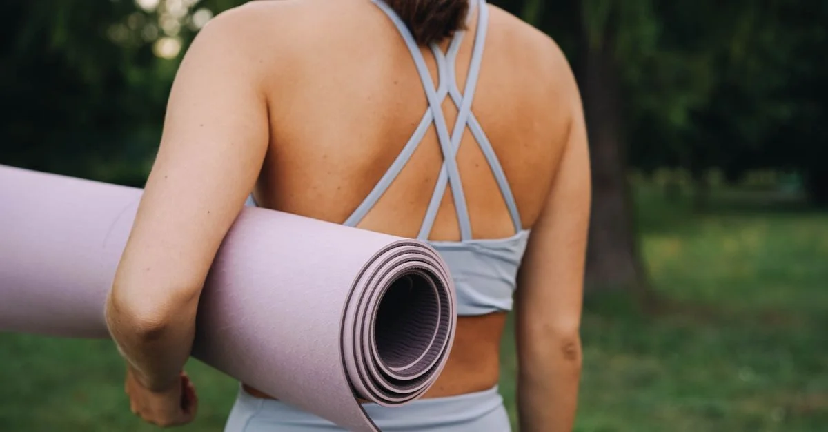 Vue de dos d'une femme tenant un tapis de yoga dans un cadre extérieur paisible.